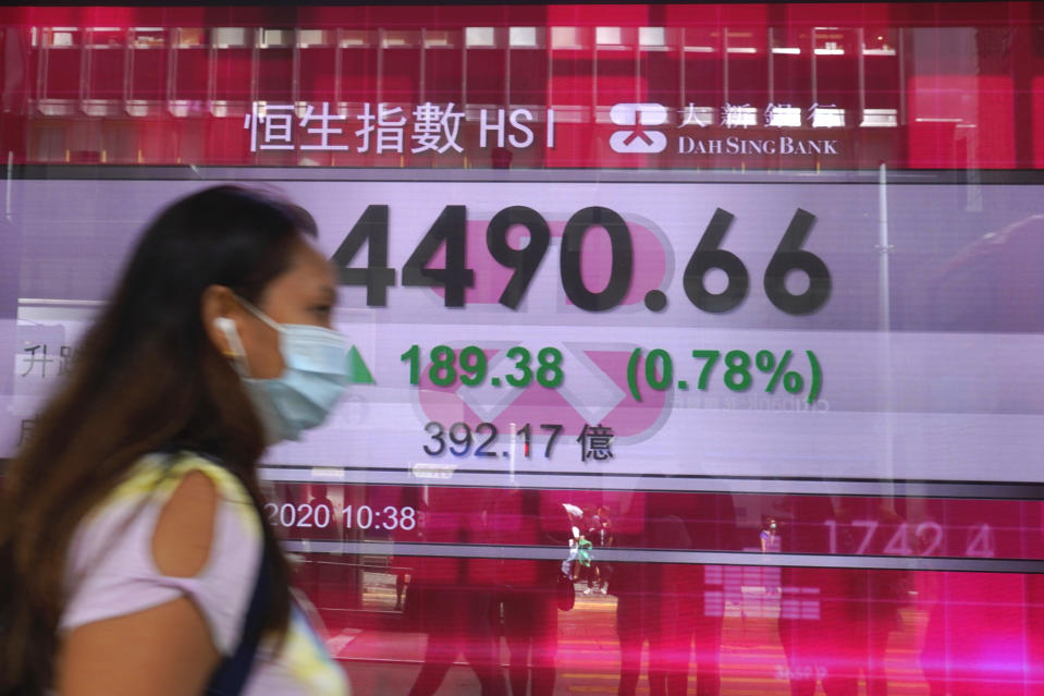 A woman wearing a face mask walks past a bank's electronic board showing the Hong Kong share index at Hong Kong Stock Exchange Tuesday, June 30, 2020. Asian shares are rising, cheered by a rally on Wally Street that underlined some optimism about global business performance despite the ongoing coronavirus pandemic. (AP Photo/Vincent Yu)