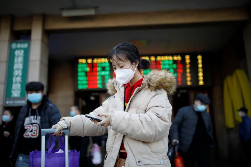 Woman wearing a face mask uses her cellphone as she walks outside Beijing Railway Station as the country is hit by an outbreak of the new coronavirus, in Beijing