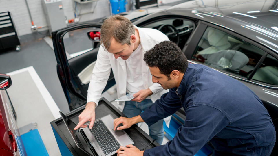 Team of mechanics working together at an auto repair shop using a computer to fix a car.