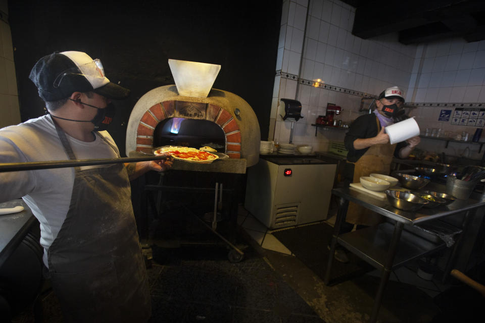 Olinser Santos, left, and Eduardo Loyola, wearing masks against the spread of the new coronavirus, prepare pizzas to go at Zaza Pizzeria in Mexico City, Friday, Dec. 18, 2020. After months of resisting to avoid hurting the economy, officials announced Friday that Mexico City and the surrounding State of Mexico will ban all non-essential activities and return to a partial lockdown starting Dec. 19 because of a spike in coronavirus cases. (AP Photo/Marco Ugarte)