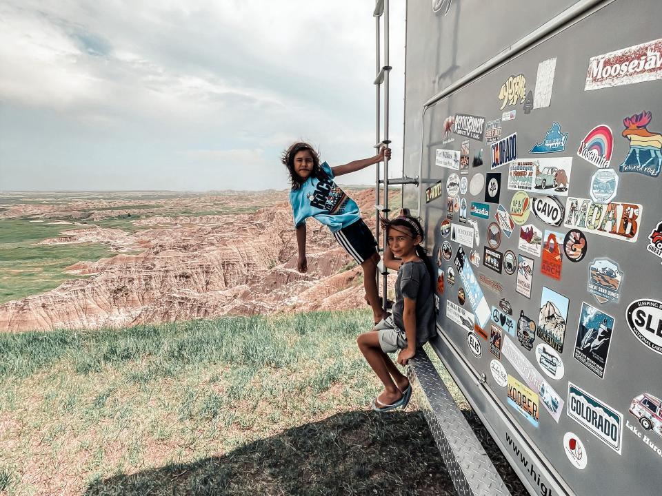 Kids posing on side of large gray RV home with bumper stickers