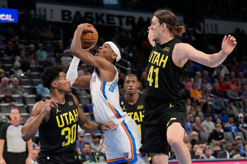 Oklahoma City Thunder guard Shai Gilgeous-Alexander, center, drives between Utah Jazz guard Ochai Agbaji (30) and forward Kelly Olynyk (41) in the first half of an NBA basketball game Sunday, March 5, 2023, in Oklahoma City. (AP Photo/Sue Ogrocki)