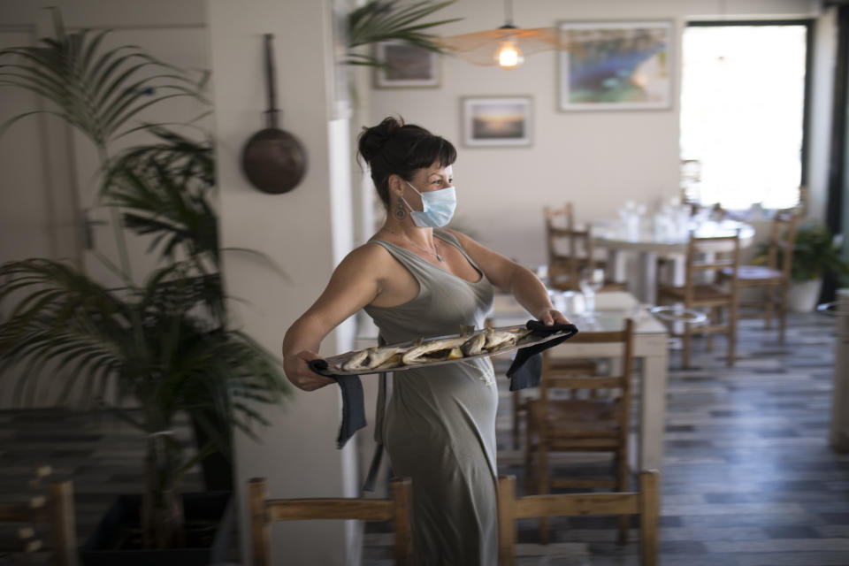 A waitress wearing a face mask to protect against coronavirus carries out a plate of fish to serve at a seafood restaurant in Marseille, southern France, Tuesday, June 2, 2020. The French way of life resumes Tuesday with most virus-related restrictions easing as the country prepares for the summer holiday season amid the pandemic. (AP Photo/Daniel Cole)