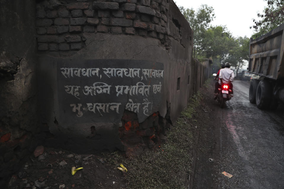 In this Oct. 23, 2019, photo, a motorist rides past a warning painted on a wall informing people about the burning coal mine zone and land subsidence near the village of Rajapur in Jharia, a remote corner of eastern Jharkhand state, India. The fires started in coal pits in eastern India in 1916. More than a century later, they are still spewing flames and clouds of poisonous fumes into the air, forcing residents to brave sizzling temperatures, deadly sinkholes and toxic gases. (AP Photo/Aijaz Rahi)