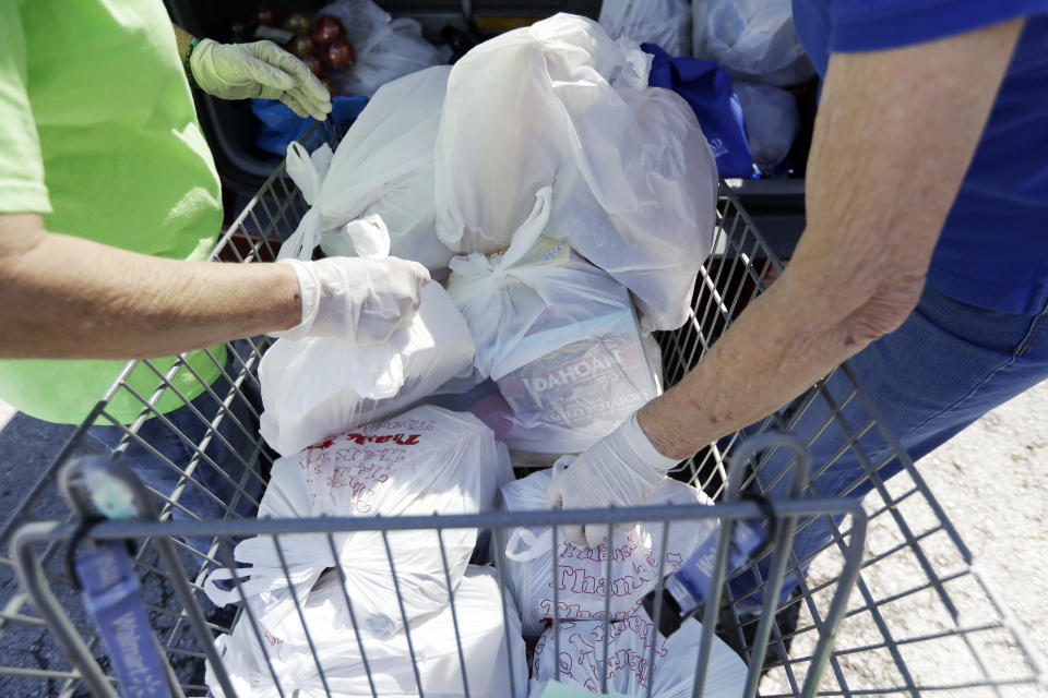 In this April 9, 2020, photo, workers remove items from a cart to load in a family's trunk at GraceWorks Ministries food pantry in Franklin, Tenn. The coronavirus pandemic has provoked a spike in demand for food pantries in the U.S. Providers have seen people lining up hours before pantries open, with cars stretching sometimes for miles. (AP Photo/Mark Humphrey)