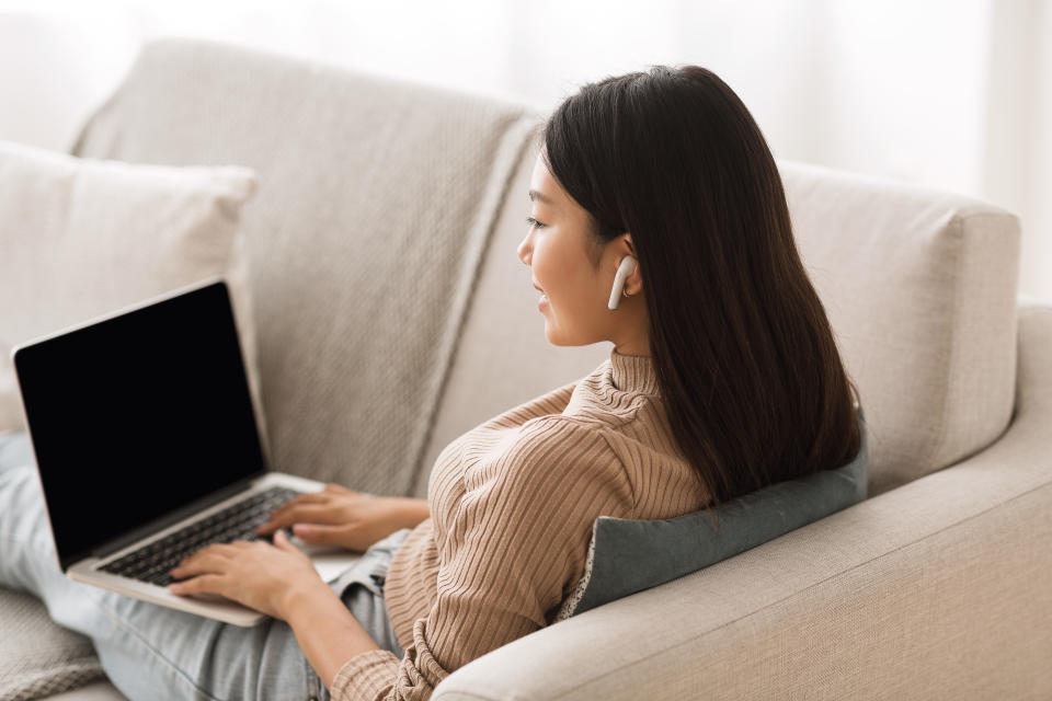 Asian girl studying online on laptop and listening music in airpods at home