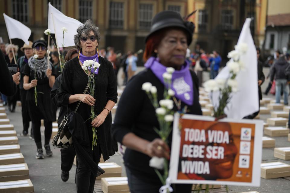 Women hold flowers and walk among boxes representing symbolic coffins as they remember former guerrillas and social leaders who have been killed since the 2016 signing of a peace agreement between rebels of the Revolutionary Armed Forces of Colombia, FARC, and the government, in Bogota, Colombia, Tuesday, Feb. 20, 2024. (AP Photo/Fernando Vergara)