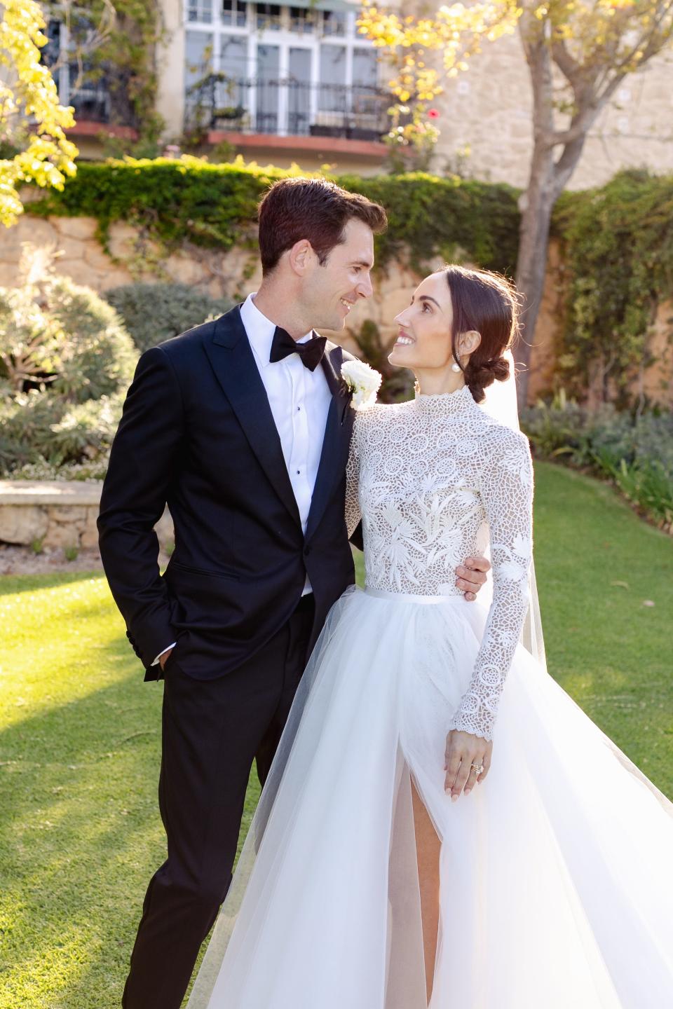 A bride and groom smile at each other in their wedding attire.