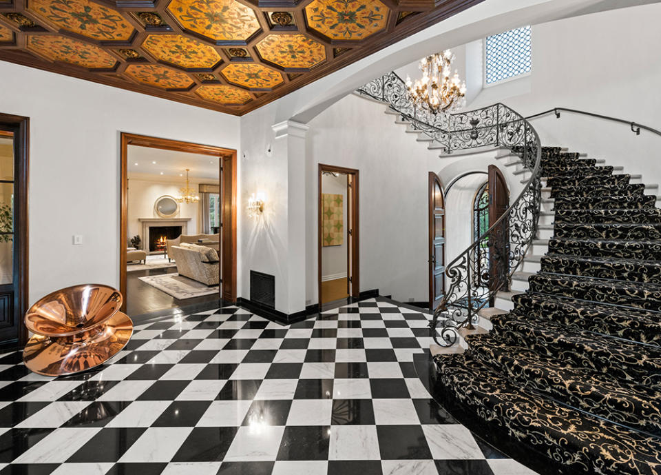The grand entry foyer displays a checkerboard-patterned marble floor and winding staircase.