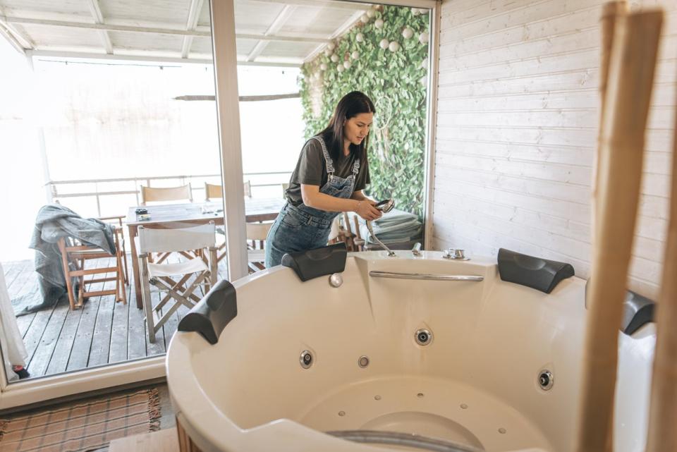 A woman holding the shower nozzle of an empty indoor hot tub.