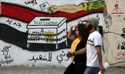 Egyptians walk past graffiti depicting a chained ballot box being controlled by the ruling military council at Tahrir Square in Cairo