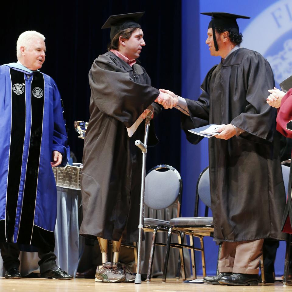 The president of Fisher College Dr. Thomas McGovern, left, watches as Boston Marathon bombing survivor Jeff Bauman, center, shakes hands with Carlos Arredondo after each received an honorary degree during commencement ceremonies in Boston, Saturday, May 10, 2014. Bauman lost his legs in the attack. He told graduates at Fisher College in Boston on Saturday to keep moving forward and seize the opportunities that lie ahead. Arredondo helped save Bauman's life that day and stressed the importance of community and teamwork. (AP Photo/Michael Dwyer)