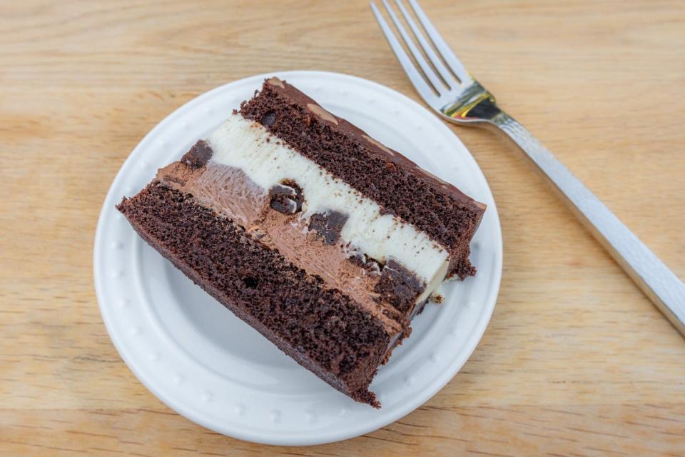 Slice of chocolate cake with chocolate cake, chocolate frosting, white frosting and chocolate layers on a plate next to a fork
