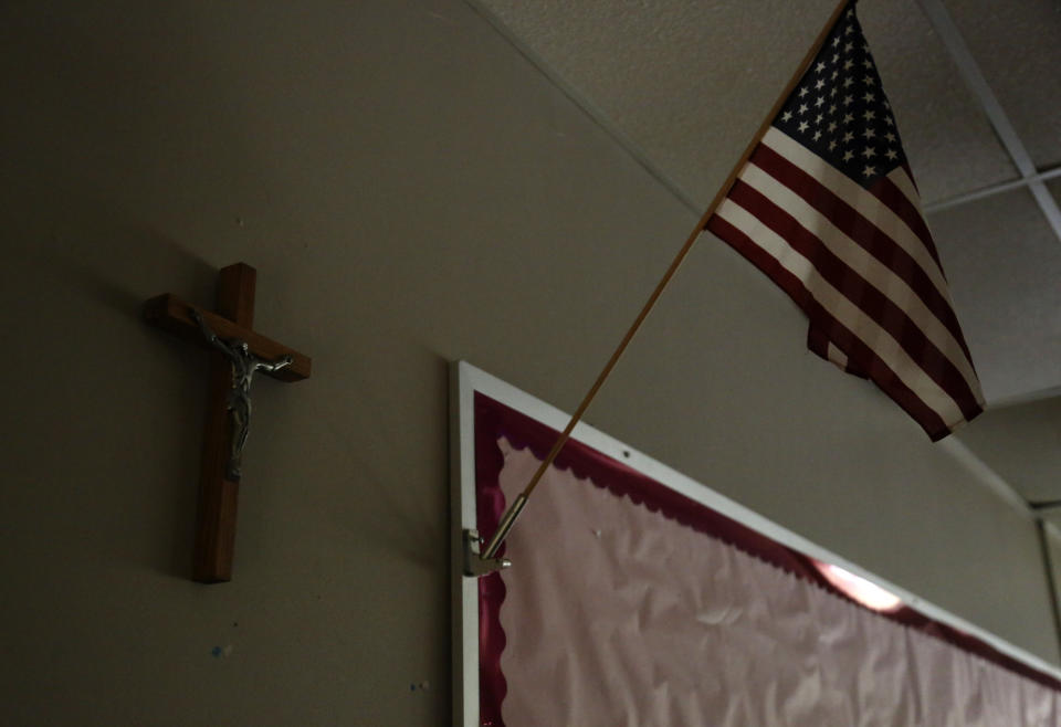 A cross hangs on the wall next to a U.S. flag in an empty classroom at Quigley Catholic High School in Baden, Pa., Monday, June 8, 2020. (AP Photo/Jessie Wardarski)