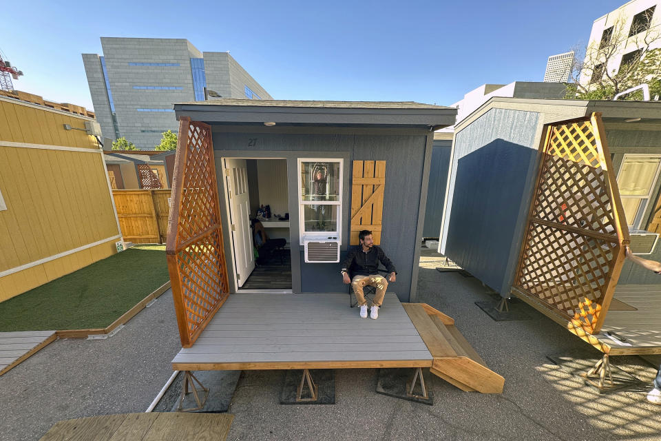 Eric Martinez sits outside of his room at a micro community in Denver on Wednesday, June 5, 2024. Martinez along with the others were directed into the micro communities of small cabin-like structures with a twin bed, desk and closet, after his Denver tent encampment was swept. The city built three such communities with nearly 160 units total in about six months, at roughly $25,000 per unit. (AP Photo/Thomas Peipert)