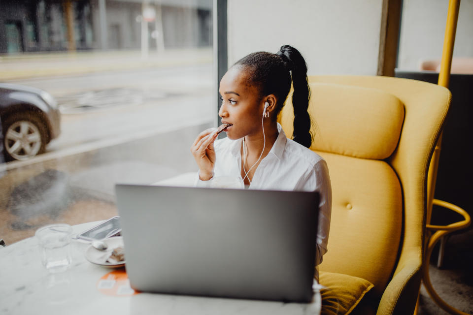 Young, stylish  African-American business woman eating cookie at the café while having a break from working on her laptop.