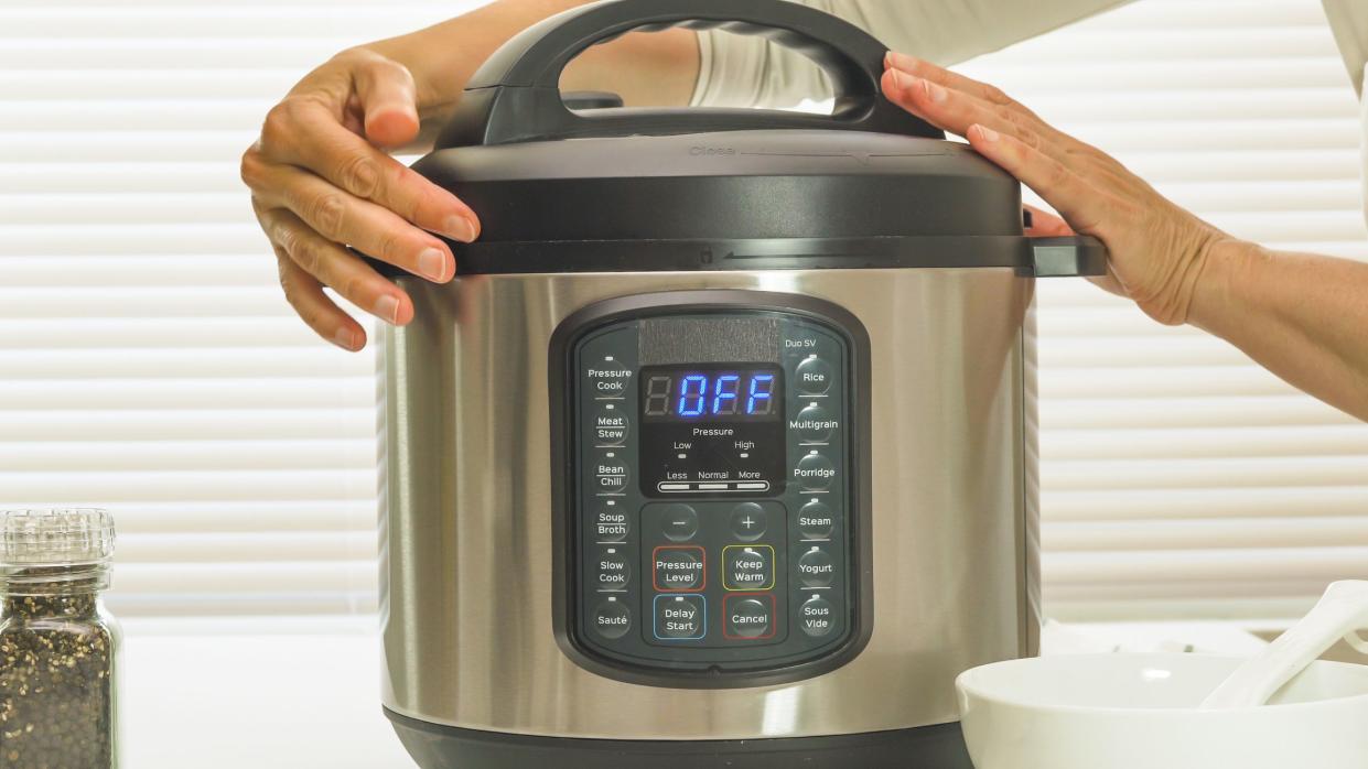 Multi cooker close up on kitchen table. Woman lifting the lid