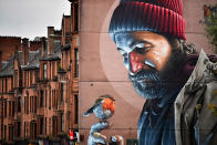 <p>A bird perches on a man’s finger in one of the latest murals near Glasgow cathedral. The murals have been appearing across the city for a since 2008. (Jeff J Mitchell/Getty Images) </p>