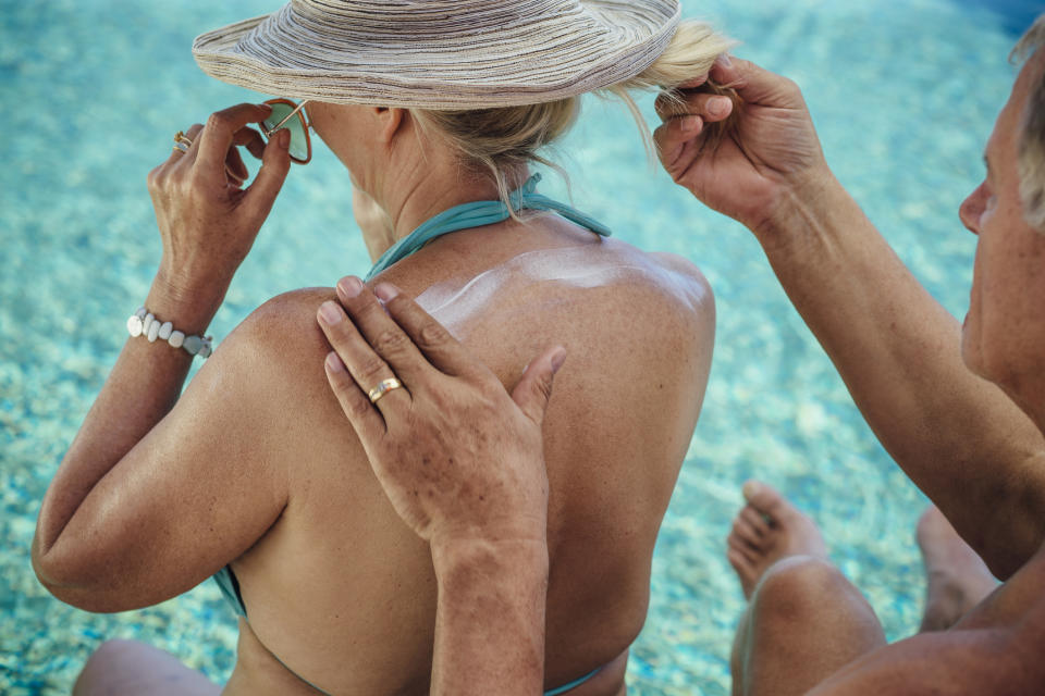 mature woman rubbing sunscreen on back to prevent skin cancer