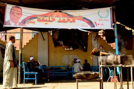 People sit at a coffee shop near a election banner for parliamentary candidate Mohamed Khalifa at a village in Minya governorate, south of Cairo, Egypt, October 8, 2015. REUTERS/Stringer