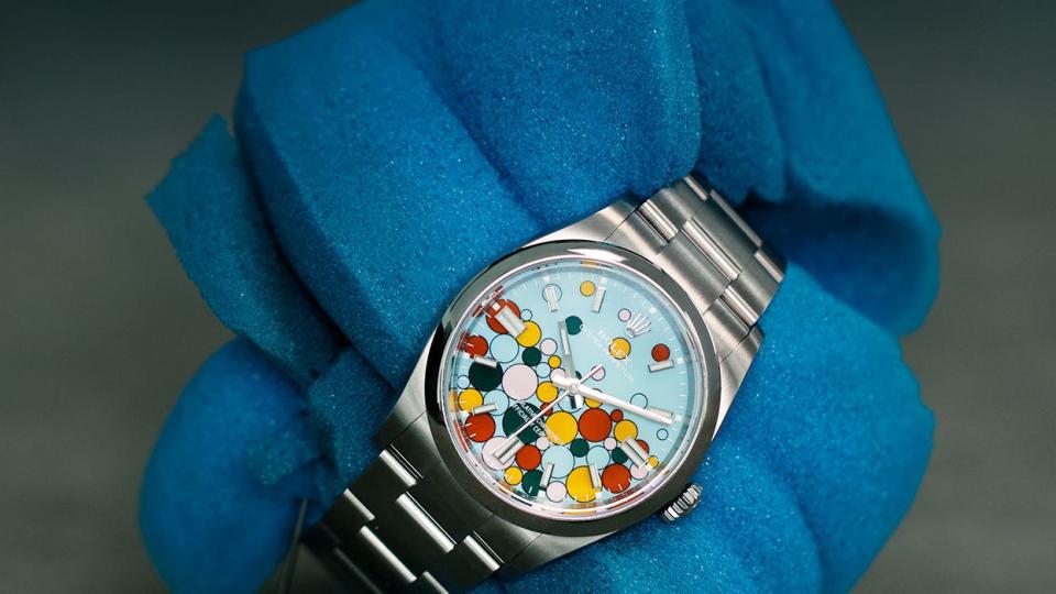 silver tone watch with colorful balloons on face of watch wrapped around a piece of blue foam