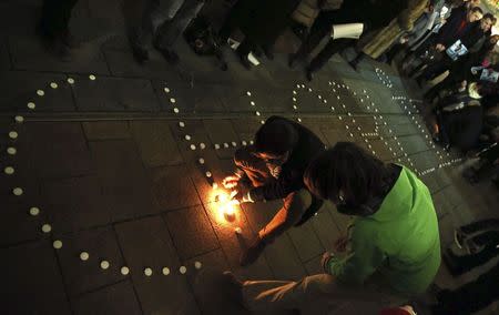 People try to light candles to form the word "Charlie" to pay tribute to the victims of a shooting by gunmen at the offices of weekly satirical magazine Charlie Hebdo in Paris, in front of the European Parliament in Brussels January 7, 2015. REUTERS/Francois Lenoir