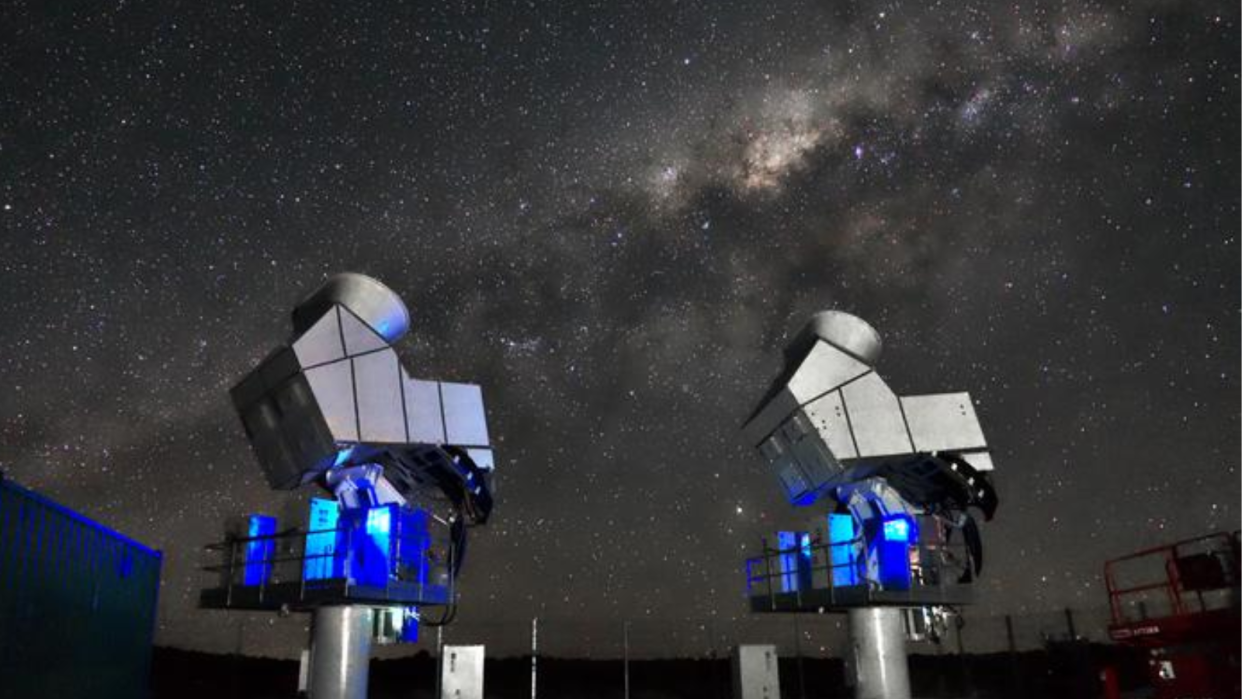  Two metal devices with blue lights at their necks are pointed up toward the sky. In the sky, there are lots of stars and the center of the Milky Way is visible. 