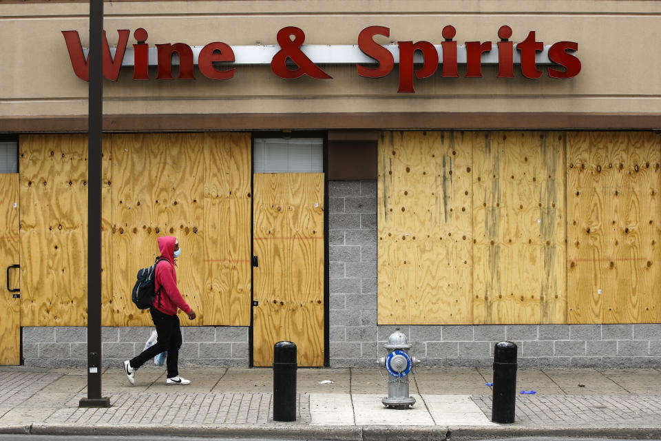 A person wearing a protective face mask as a precaution against the coronavirus walks past a boarded up Wine and Spirits store in Philadelphia, Thursday, April 16, 2020. Pennsylvania's liquor agency says workers are coming back on the job at more than 100 shuttered state-owned liquor stores to help process online orders. (AP Photo/Matt Rourke)