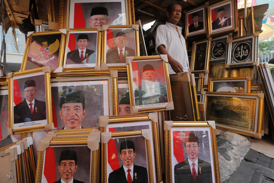 In this Wednesday. Oct. 16, 2019, photo, a man walks past portraits of Indonesian President Joko Widodo and Vice President-elect Ma'ruf Amin displayed at a stall in Jakarta, Indonesia. Known for his down-to-earth style with a reputation for clean governance, Widodo's signature policy has been improving Indonesia's inadequate infrastructure and reducing poverty, which afflicts close to a tenth of Indonesia's nearly 270 million people. But raising money would be harder at a time of global economic slowdown, major trade conflicts and falling exports. (AP Photo/Tatan Syuflana)