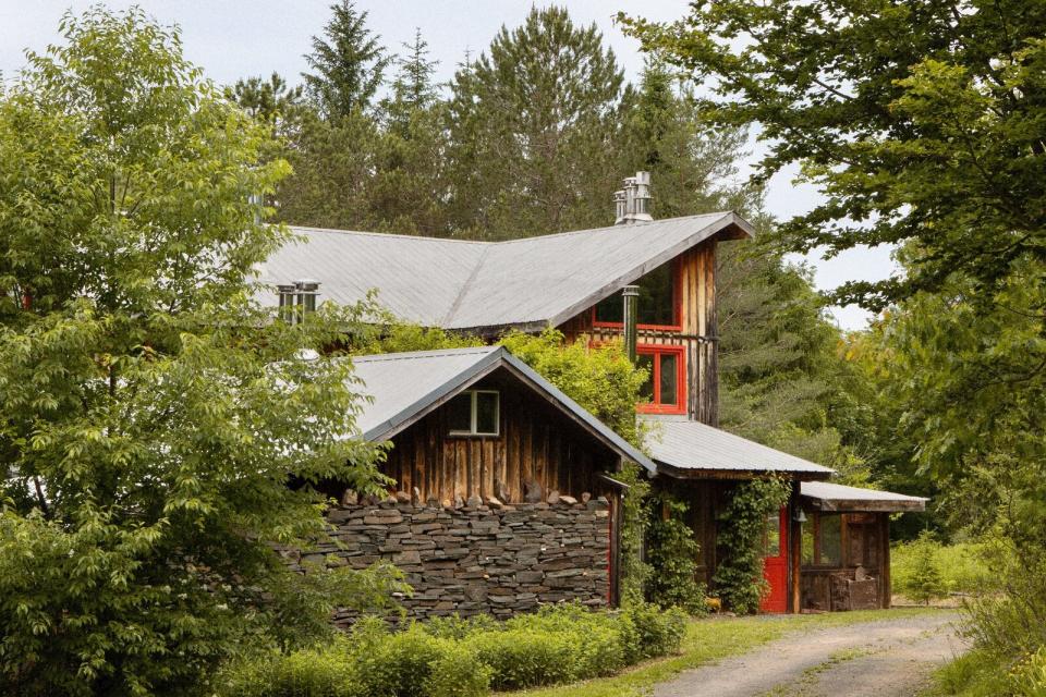 The well-preserved wood-and-stone-clad home rests at the end of a long, gravel drive, surrounded by a mature forest. Its bright red door extends a cheerful welcome.