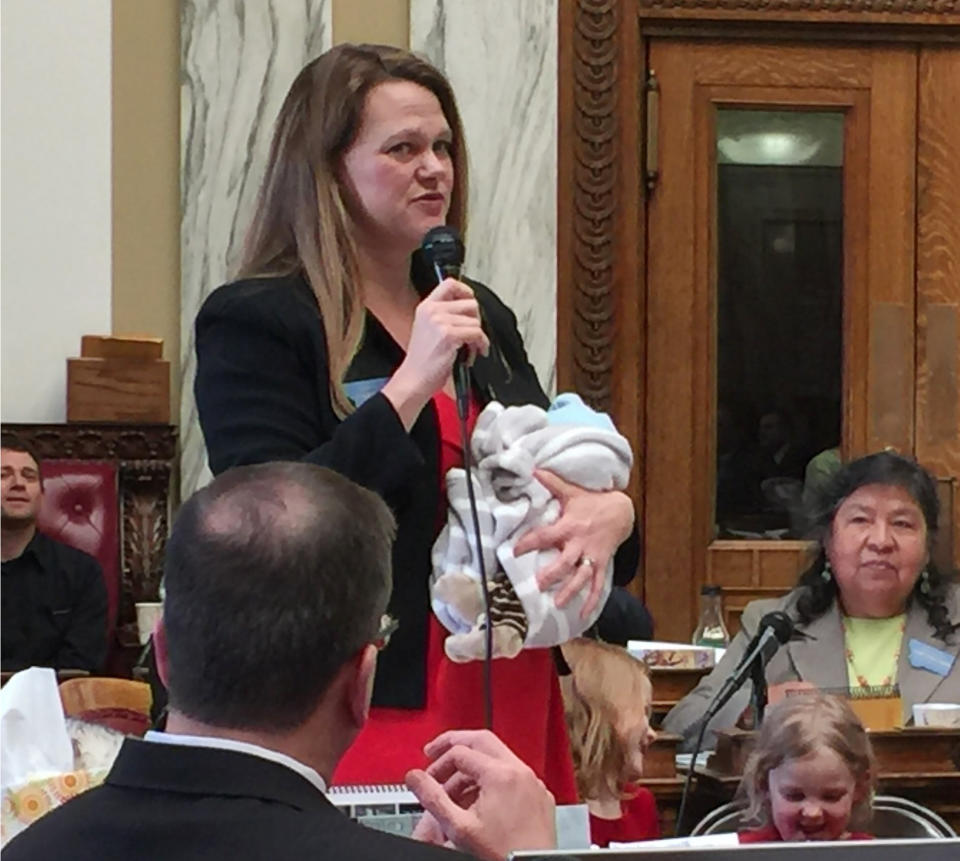 In this March 2017, photo, provided by Rep. Kimberly Dudik, Dudik speaks on the floor of the legislature holding her newborn son Marcutio in Helena, Mont. As experts predict another banner year of women running for office, hurdles remain particularly for those like Dudik who have young children. Only six states have laws specifically allowing the use of campaign funds for child care. In most states, including Montana, the law is silent on the issue and up to interpretation by state agencies or boards. (Rep. Nate McConnell/Rep. Kimberly Dudik via AP)