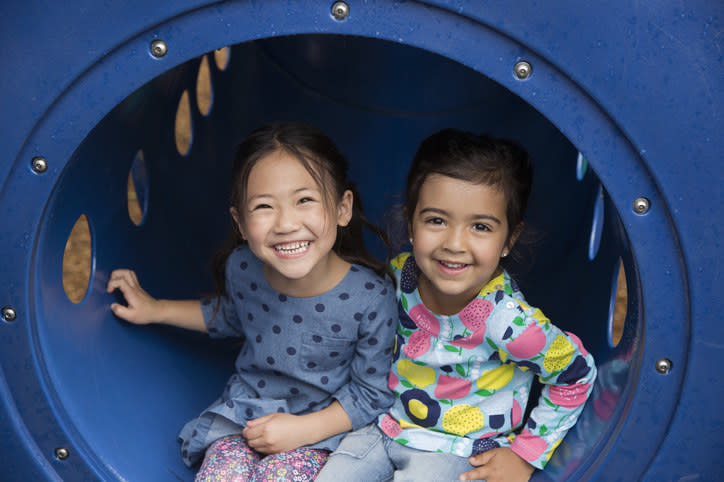 Portrait of two girls sitting in playground tunnel and smiling