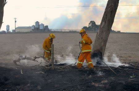 Firefighters use water to put out spot fires near a farm on the outskirts of the town of Cobden, located south west of Melbourne, Australia March 18, 2018. AAP/David Crosling/via REUTERS