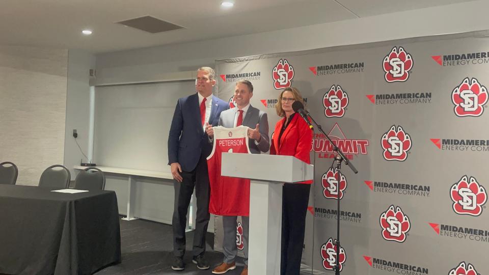 New South Dakota men's basketball coach Eric Peterson holds up a jersey between Athletic Director David Herbster and South Dakota president Sheila Gestring on Wednesday, March 16, 2022.