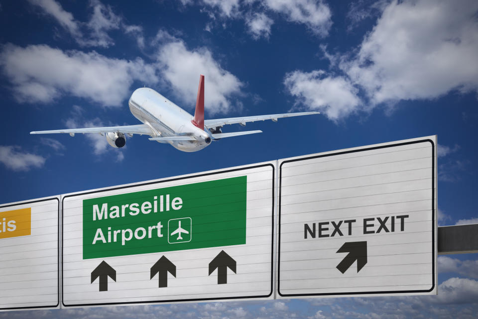 Airplane flying over freeway signage directing to Marseille Airport, indicating the next exit