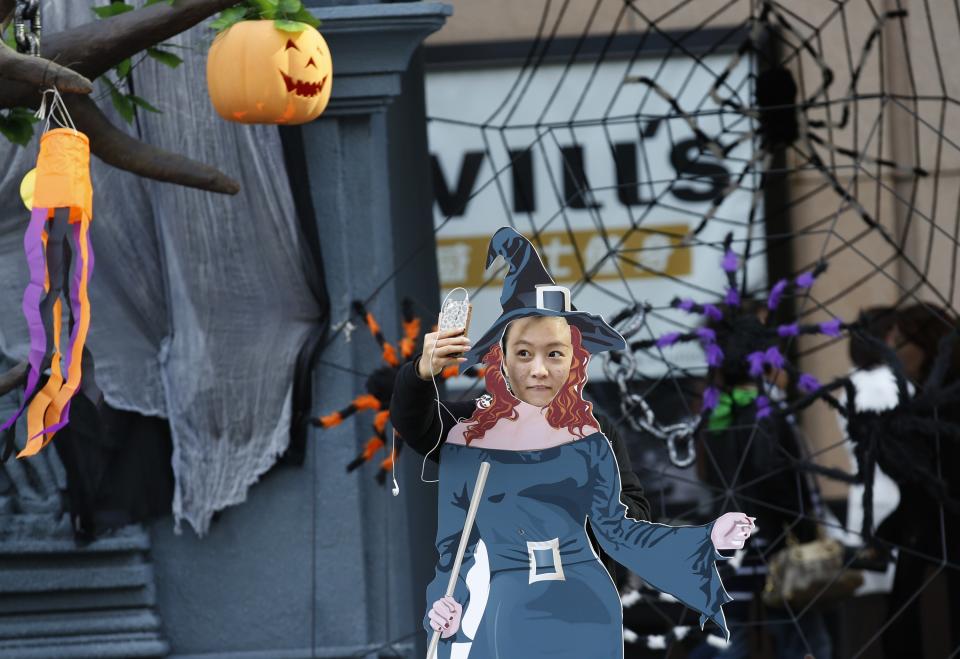 A woman takes a picture of herself with her phone as she poses behind a cardboard cutout symbolising a witch at an event for the upcoming Halloween Day outside a shopping mall in Beijing, October 23, 2013. REUTERS/Kim Kyung-Hoon (CHINA - Tags: SOCIETY)