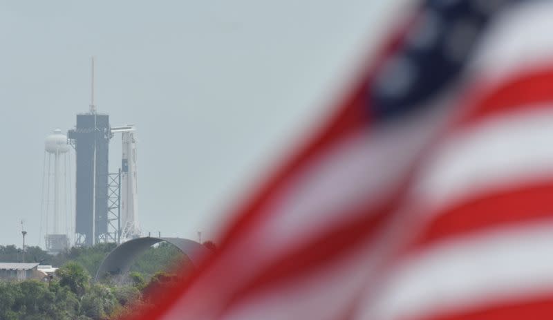 A U.S. flag flutters in the breeze as the SpaceX Crew Dragon on a Falcon 9 booster rocket sits on Pad39A