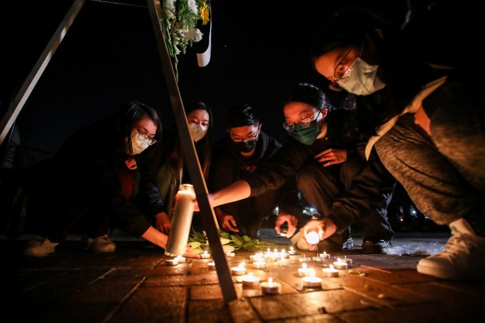 Seen from a low angle, five young Asian people squat to light tea candles.