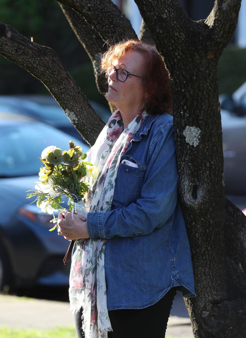 Kim Shaver held flowers as she leaned against a tree in the distance during a vigil at the Crescent Hill Presbyterian Church to honor the victims of the mass shooting at the Old National Bank earlier in the day in Louisville, Ky. on Apr. 10, 2023.  