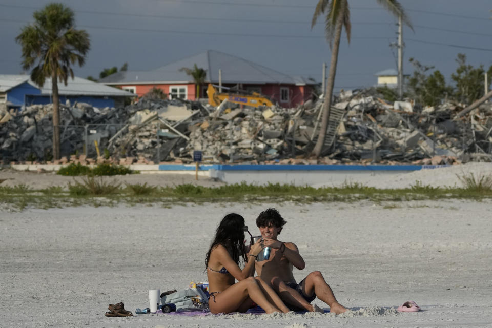 Eighteen-year-old Gioia Fallon, left, and Robby Hildebrand, who grew up in Fort Myers and have been coming to the beach since they were kids, drink a toast as they sit in front of a backdrop of demolished buildings, in Fort Myers Beach, Fla., Wednesday, May 10, 2023. "Probably the biggest challenge is the craziness of the debris removal process," said Chris Holley, former interim Fort Myers Beach town manager. "We'll be at it for another six months." (AP Photo/Rebecca Blackwell)