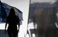 FILE - In this Wednesday, Aug. 19, 2020 file photo, a woman walks toward EU flags as she is reflected in the marble of the European Commission building in Brussels. The European Union executive announced Thursday, March 4, 2021 that it wants to force employers to be much more open about how much money staff makes to make it easier for women to challenge wage imbalances and further closer the gender pay gap. The EU made it clear that women workers had been disproportionally affected by the pandemic, many having to add more home tasks to their work schedule because of closure of schools and day care centers. (AP Photo/Virginia Mayo, File)