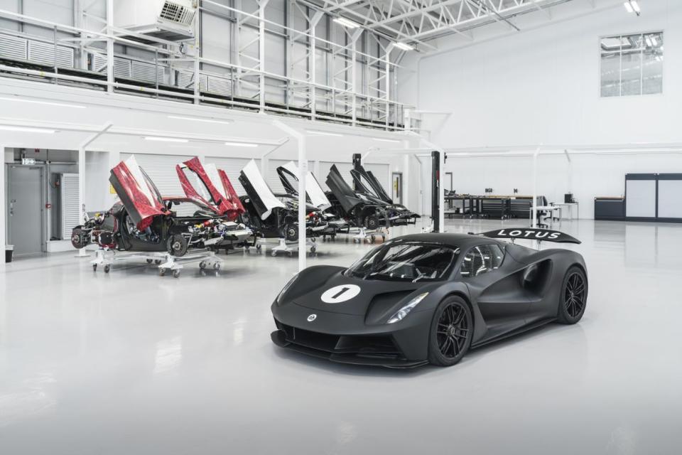 Image of the Lotus Evija production hall with a series of half-completed models in the background, while in the foreground a black Evija in racing livery sits.