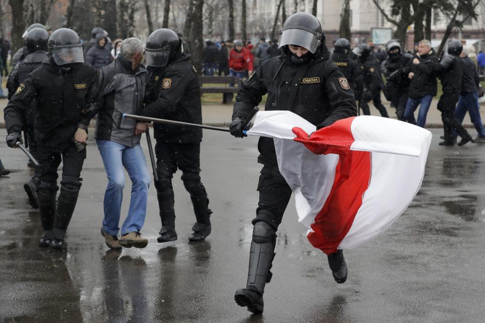 A Belarus policeman runs with an opposition flag as other detain a protester during an opposition rally in Minsk, Belarus, Saturday, March 25, 2017. A cordon of club-wielding police blocked the demonstrators' movement along Minsk's main avenue near the Academy of Science. Hulking police detention trucks were deployed in the city center. (AP Photo/Sergei Grits)