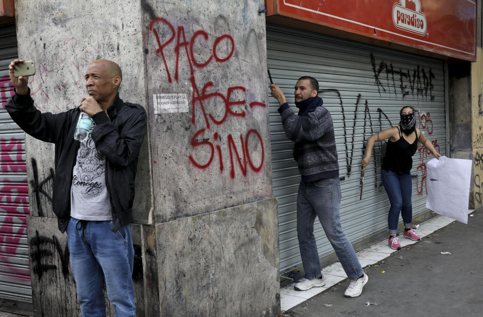 A man takes images with his smart phone as anti-government demonstrators take cover during clashes with the police in Santiago, Chile, Wednesday, Oct. 23, 2019. Tens of thousands of protesters have taken to the streets Chile's capital as an apology and promises of reform from President Sebastián Piñera failed to quell turmoil that has led to looting, rioting and at least 18 deaths. (AP Photo/Rodrigo Abd)