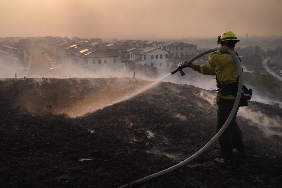 Firefighter Tylor Gilbert puts out hotspots while battling the Silverado Fire, Monday, Oct. 26, 2020, in Irvine, Calif. A fast-moving wildfire forced evacuation orders for 60,000 people in Southern California on Monday as powerful winds across the state prompted power to be cut to hundreds of thousands to prevent utility equipment from sparking new blazes. (AP Photo/Jae C. Hong)