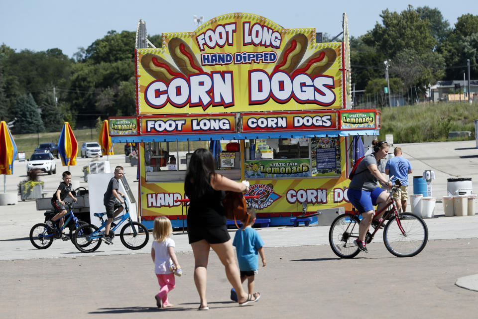 FILE - In thisJuly 28, 2020, file photo, Iowa state fairgrounds visitors pass a corn dog stand set up for the Taste of the Fair to be held this weekend in Des Moines, Iowa. Families trying to get in a last-minute vacation before school starts better do some homework on COVID-19 restrictions before loading up the minivan. (AP Photo/Charlie Neibergall, File)