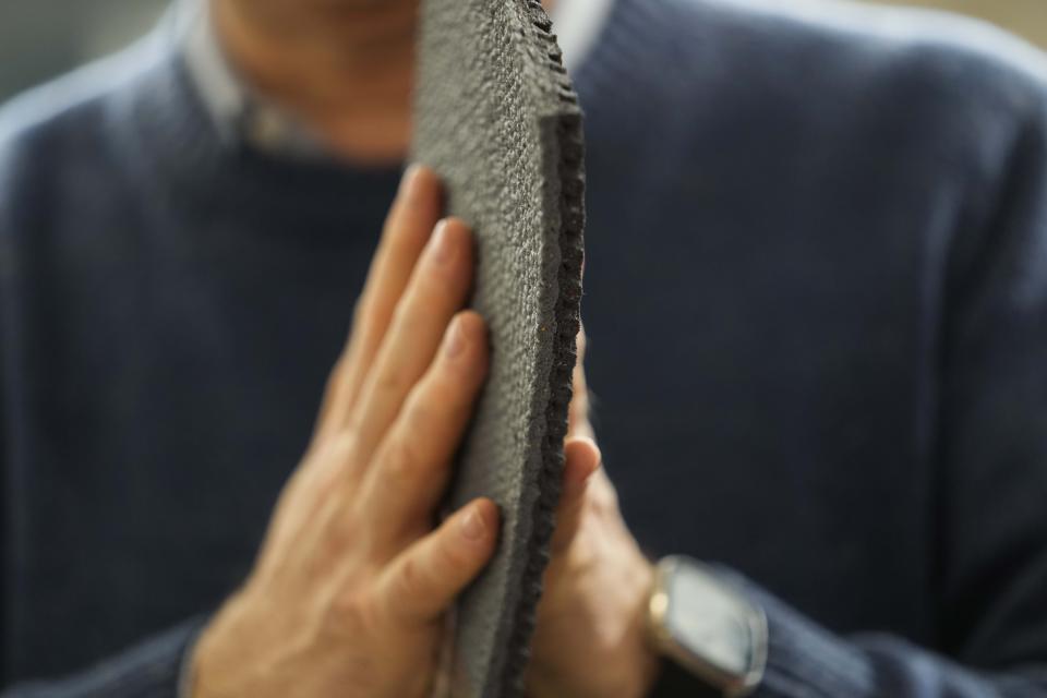 A worker shows a surface portion of an athletics track, at the Mondo factory, in Alba, northern Italy, Wednesday, March 13, 2024. The athletics track for the upcoming Paris Olympics is being produced by the Mondo company at its factory in northern Italy. The track is made in portions, rolled up and then will be transported to the Stade de France, where it will be installed over the next month. (AP Photo/Luca Bruno)