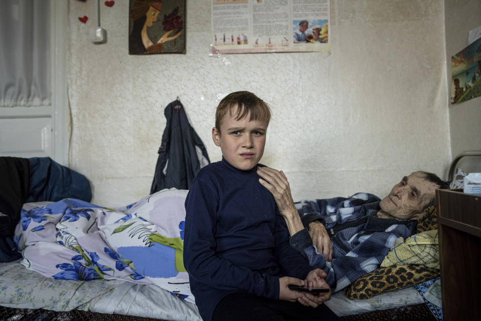 Mykola Svyryd, 70, touches the shoulder of his son Bohdan, in a shelter for injured and homeless people in Izium, Ukraine, Monday, Sept. 26, 2022. The young Ukrainian boy with disabilities, 13-year-old Bohdan, is now an orphan after his father, Mykola Svyryd, was taken by cancer in the devastated eastern city of Izium. (AP Photo/Evgeniy Maloletka)