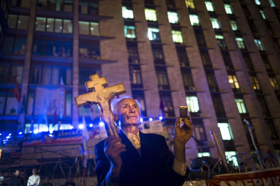 A pro-Russian man holds an Orthodox cross as a crowd are celebrating declaring independence for Donetsk region at barricades in front of a regional administration building that was seized by pro-Russian activists in Donetsk, Ukraine, Monday, May 12, 2014. Pro-Moscow insurgents in eastern Ukraine declared independence Monday and put pressure on Kiev to hold talks with the separatists. (AP Photo/Alexander Zemlianichenko)