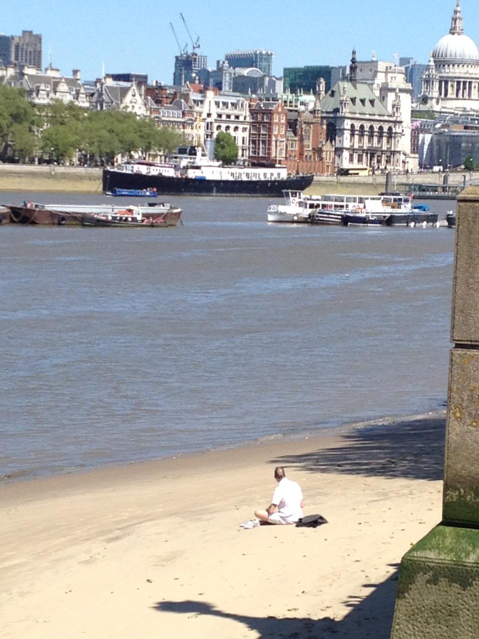 London's Southbank in summer - man sunbathes on beach by Waterloo Bridge